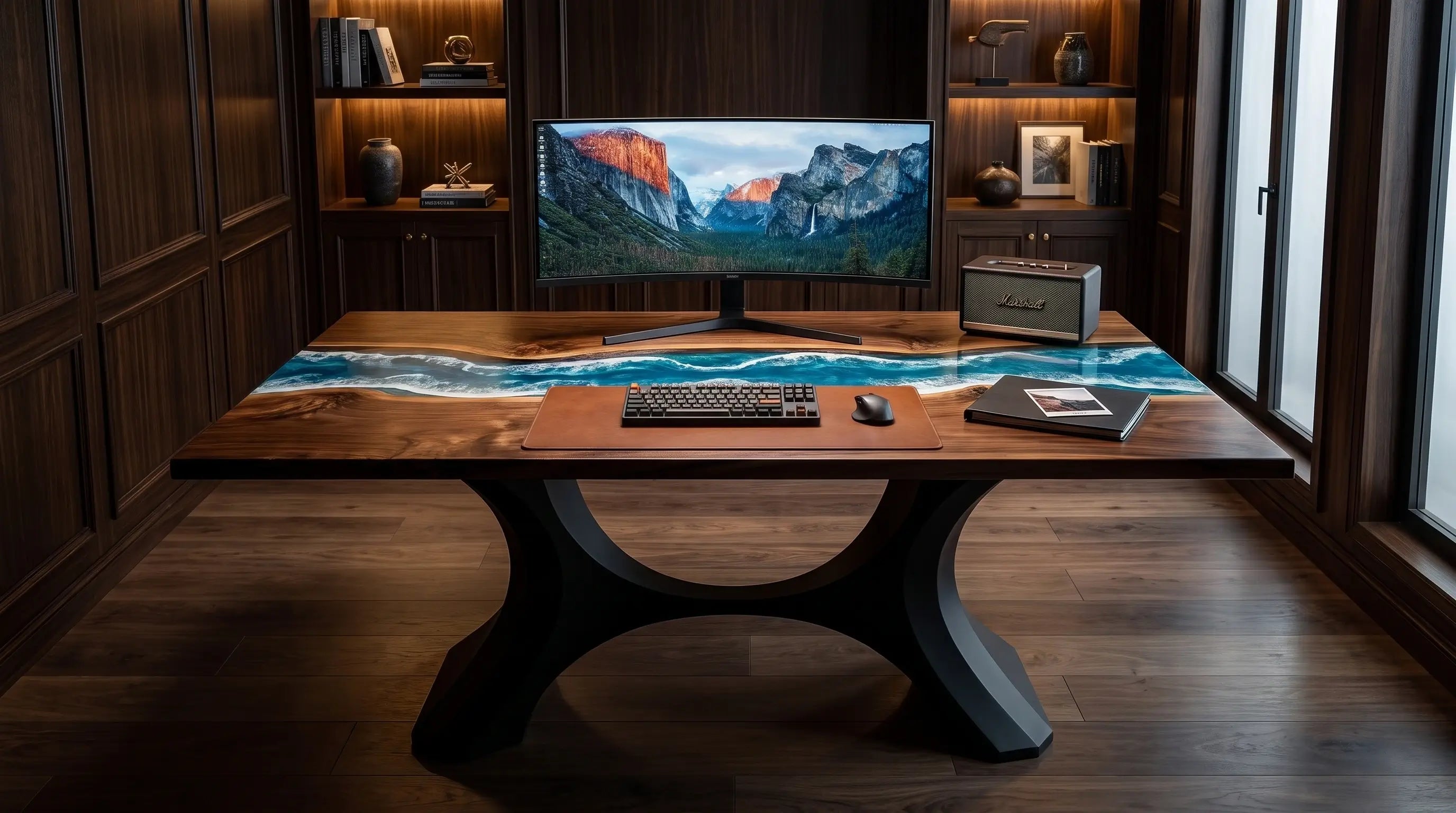 A modern wooden desk with a dramatic wave-patterned resin top and sculptural black legs, styled in a dark wood home office with a computer monitor, keyboard, and laptop on top.