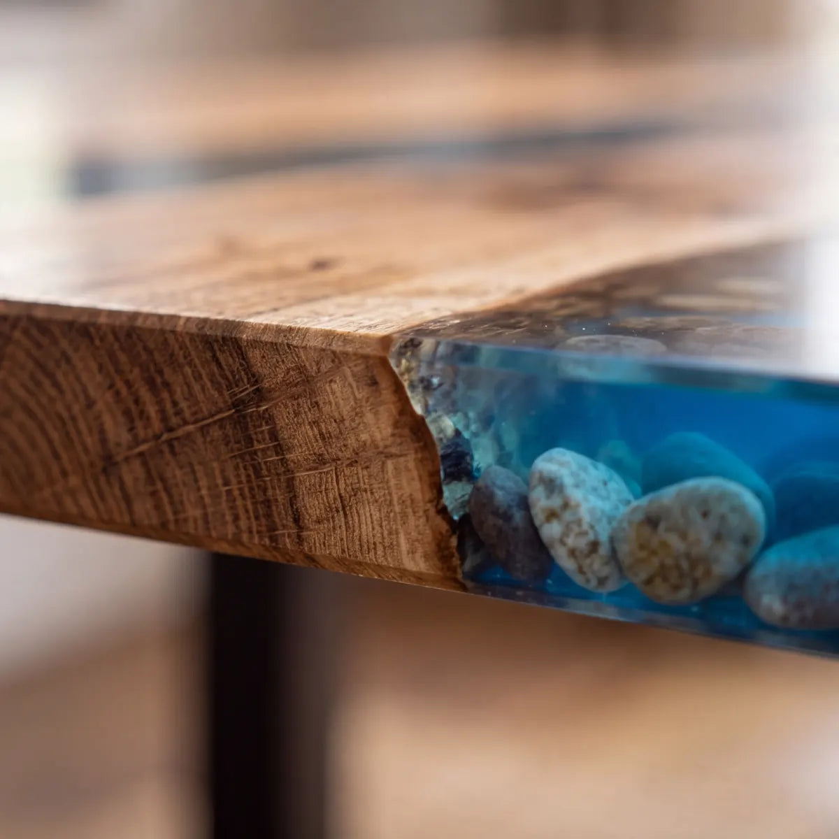 Cross-section close-up of blue epoxy river with embedded stones and wood edge